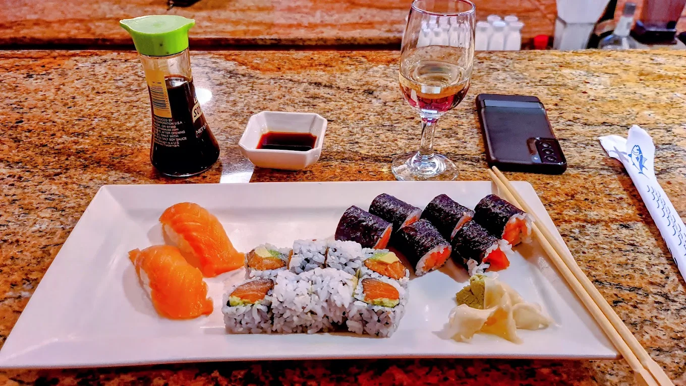 Salmon nigiri, salmon avocado rolls and salmon maki on a white plate with ginger and wasabi at the counter